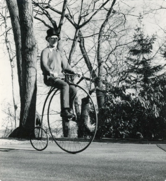 Claude Shannon riding a high wheel bicycle with trees in the background