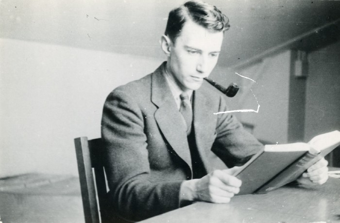 A young Claude Shannon reading a book at a desk while smoking a pipe
